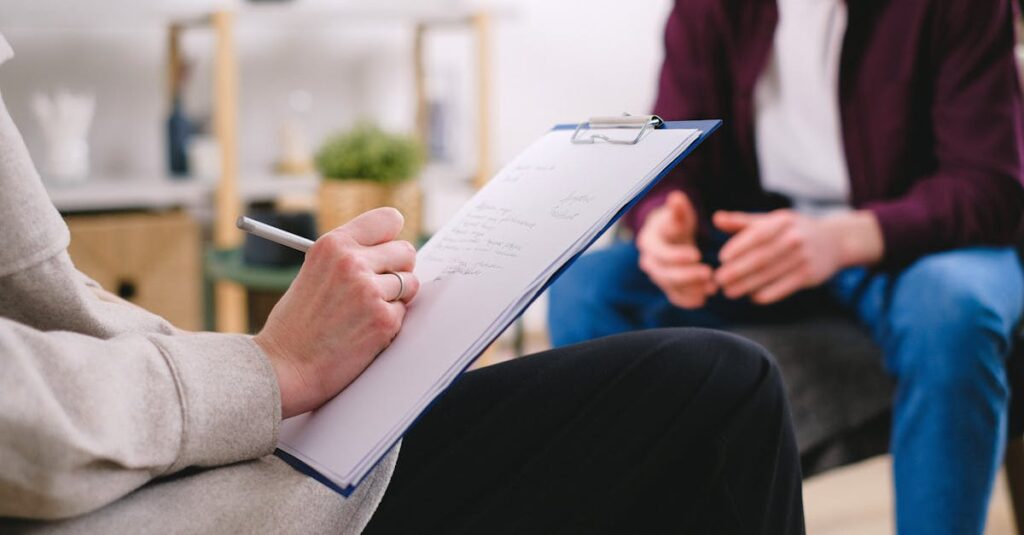 pexels-photo-7176076-7176076 Close-up of a therapist writing notes on a clipboard while conversing with a patient.