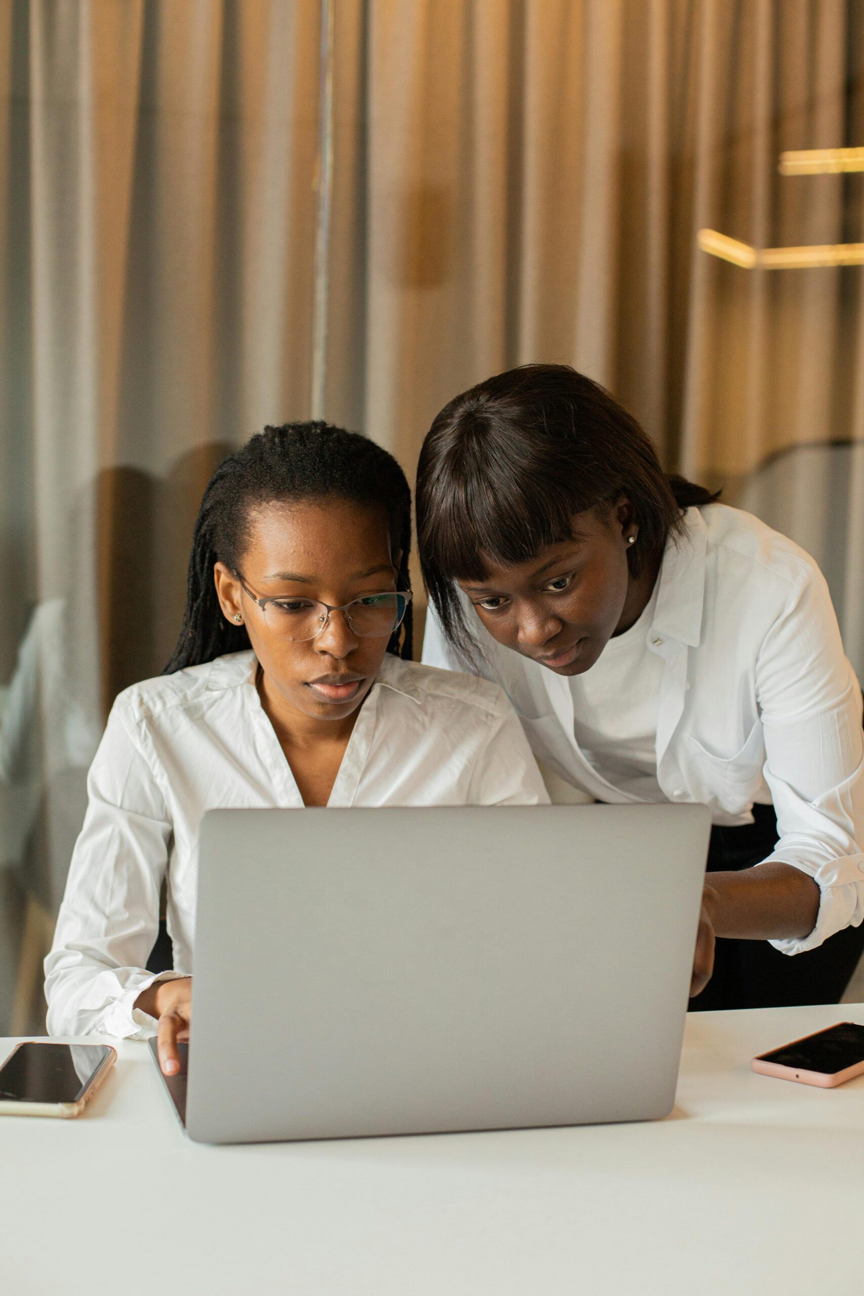 Two women in business attire working together on a laptop, fostering teamwork and cooperation.