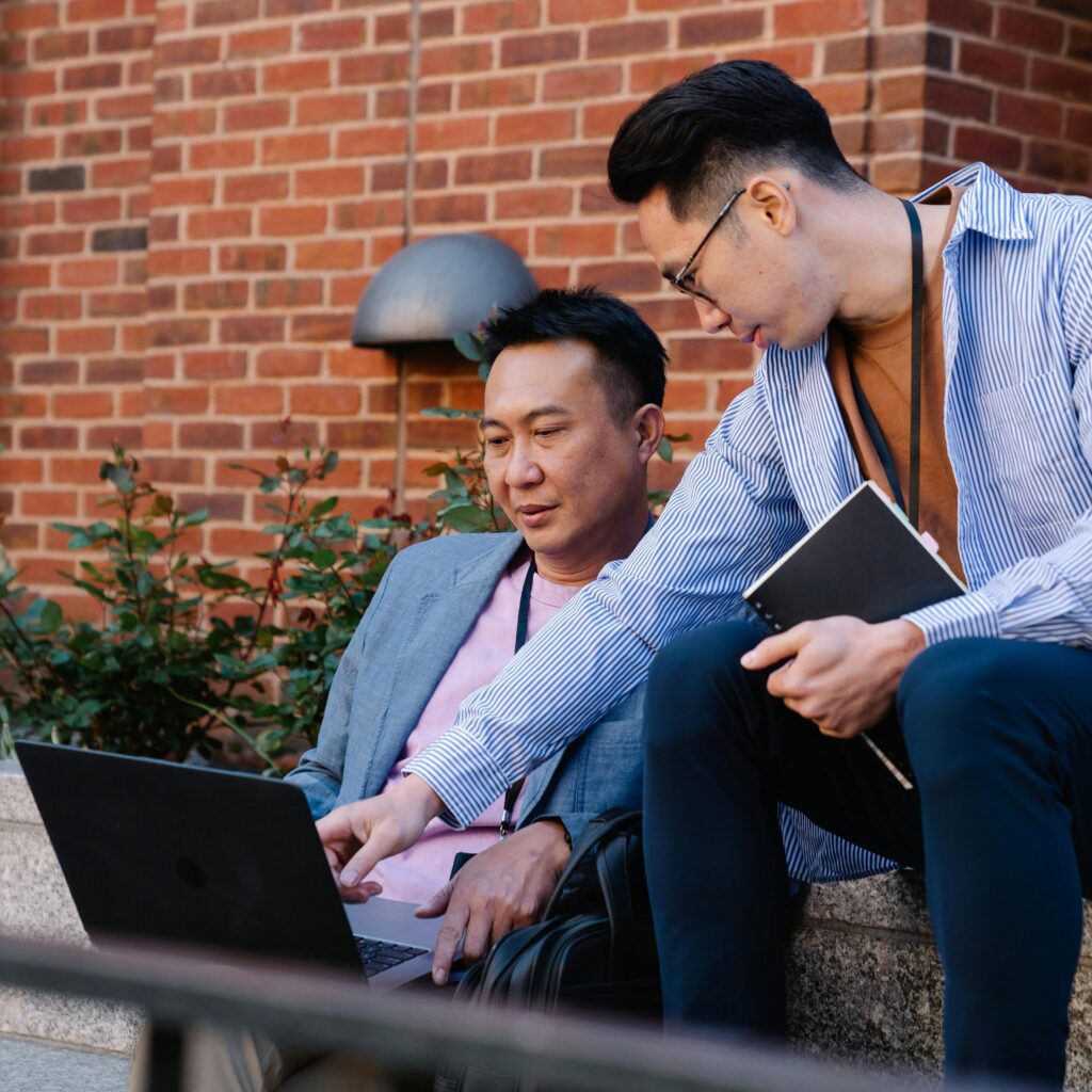 Two men collaborating on a laptop outdoors, discussing business strategies.